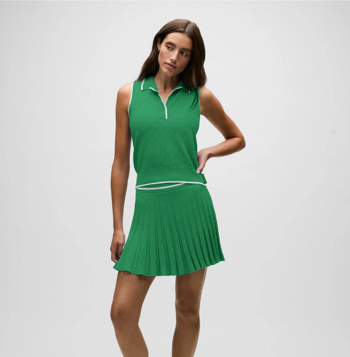 Model wearing the green sleeveless knit top with a pleated athletic skirt.