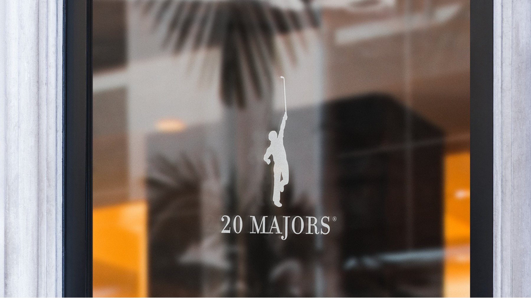 The flagship window at dusk, the golfer silhouette and 20 Majors name etched across black glass.