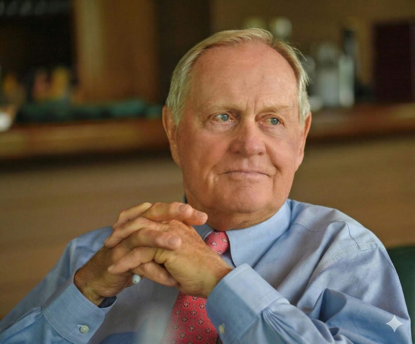 Jack Nicklaus, hands clasped, seated in a clubhouse interior.